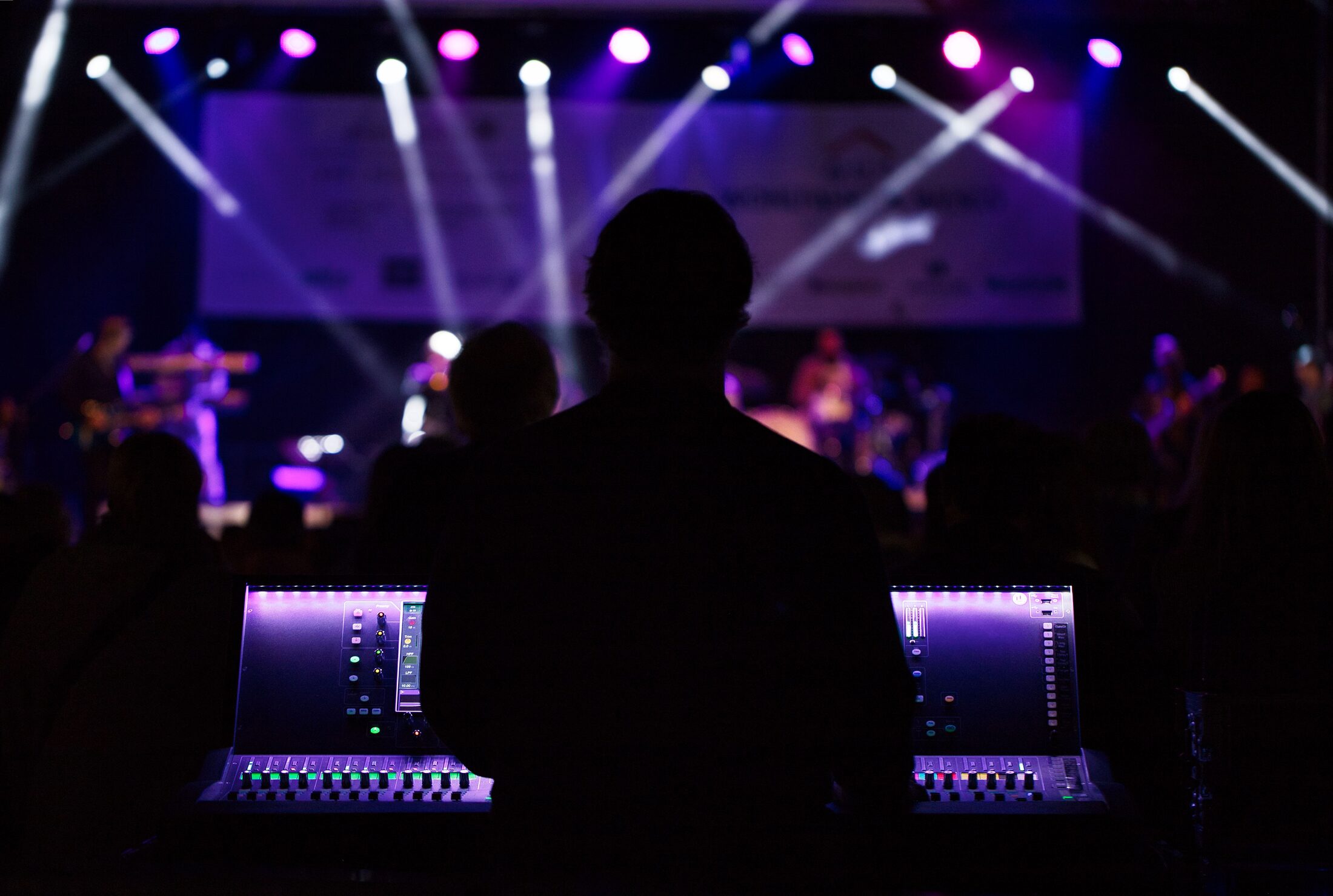 A specialist working behind the scenes at a live event, the stage and performance visible beyond